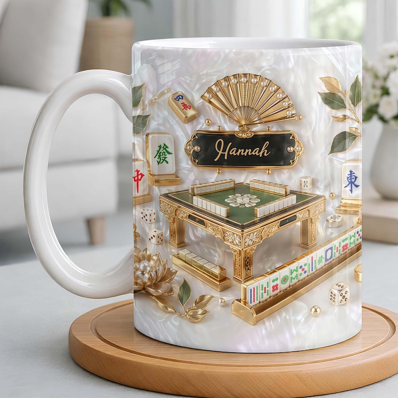 May include: White ceramic mug featuring a detailed design of a Mahjong game. The design includes a miniature table, tiles, dice, and a fan, with the name "Hannah" displayed. The mug sits on a wooden coaster.