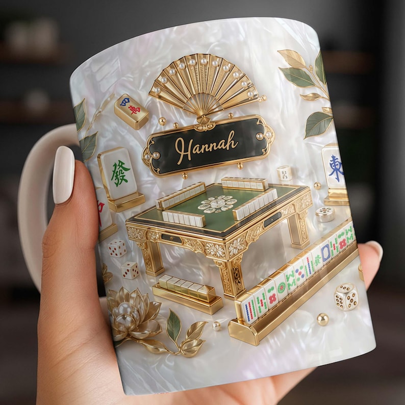 May include: White ceramic mug featuring a detailed design of a Mahjong table, tiles, dice, and a fan. The mug has a pearlescent background and the name "Hannah" is displayed on a black plaque. Gold accents enhance the design.