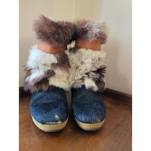 Puede incluir: Un par de botines con empeines de cuero de pelo negro, cuellos de cuero color canela y puños de piel sintética gruesa en tonos blanco, marrón y gris. Los botines cuentan con suelas de plataforma planas de color claro y aspecto gomoso.