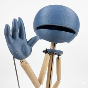 May include: A blue and wooden articulated puppet with a round head and a hand raised in a waving gesture. The puppet's head has a large opening, and its limbs are made of wood. The puppet is designed to be posed and manipulated.