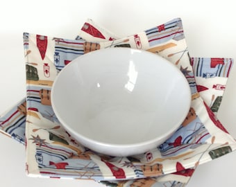 May include: A white ceramic bowl sits inside a fabric bowl holder. The holder is made of two layers of fabric with a pattern of blue and red canoes and paddles on a white background.
