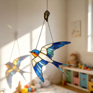 May include: A stained glass swallow bird with blue, white, and teal wings, and a blue head with orange accents. The bird is suspended by a chain from a decorative metal hook. The bird's shadow is visible on the wall.