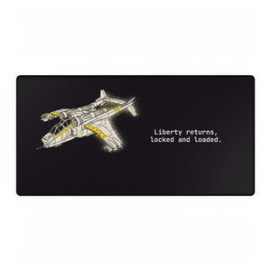 May include: Black rectangular mousepad featuring a detailed illustration of a futuristic aircraft in white and yellow. The text "Liberty returns, locked and loaded" is printed in white on the right side of the mousepad.