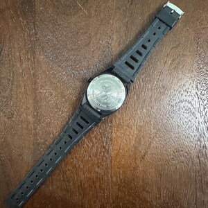 May include: A black wristwatch with a flexible rubber strap and a silver-toned stainless steel case back. The back of the watch features engraved text including the words stainless steel, water resistant, and various alphanumeric codes.