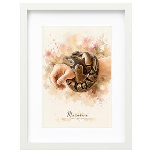 May include: A framed watercolor print featuring a brown and black patterned ball python coiled around a forearm. The artwork has a soft, splattered background in shades of beige and brown, with the word Macaroni written in cursive at the bottom.