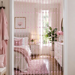 May include: A doorway beaded curtain featuring multiple vertical strands of translucent pink spherical beads. The beads are arranged in a repeating pattern of varying sizes, suspended from a horizontal rod to create a semi-transparent partition.