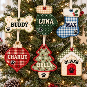 May include: Six fabric Christmas ornaments with cream ribbons. Shapes include a bone labeled BUDDY, a mitten labeled LUNA, a stocking labeled MAX, a bauble labeled CHARLIE, a tree labeled BELLA, and a house labeled OLIVER. Each features embroidered names and paw prints.