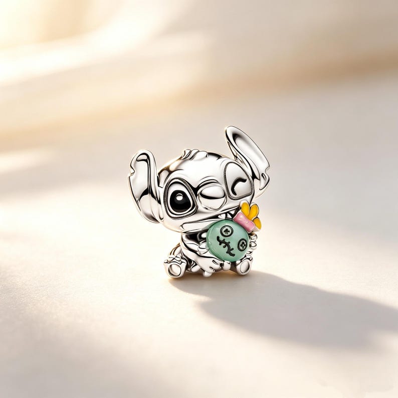 Puede incluir: Un charm de plata que representa al personaje Stitch de la pel&iacute;cula animada Lilo & Stitch. El charm gui&ntilde;a un ojo y sostiene una bola verde con una cara, acentuada con un lazo rosa y una flor amarilla.
