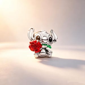 Puede incluir: Una figura plateada del personaje Stitch de Lilo & Stitch, sosteniendo una rosa roja con un tallo verde. La figura gui&ntilde;a un ojo y tiene ojos grandes y expresivos. La rosa est&aacute; detallada con p&eacute;talos visibles.