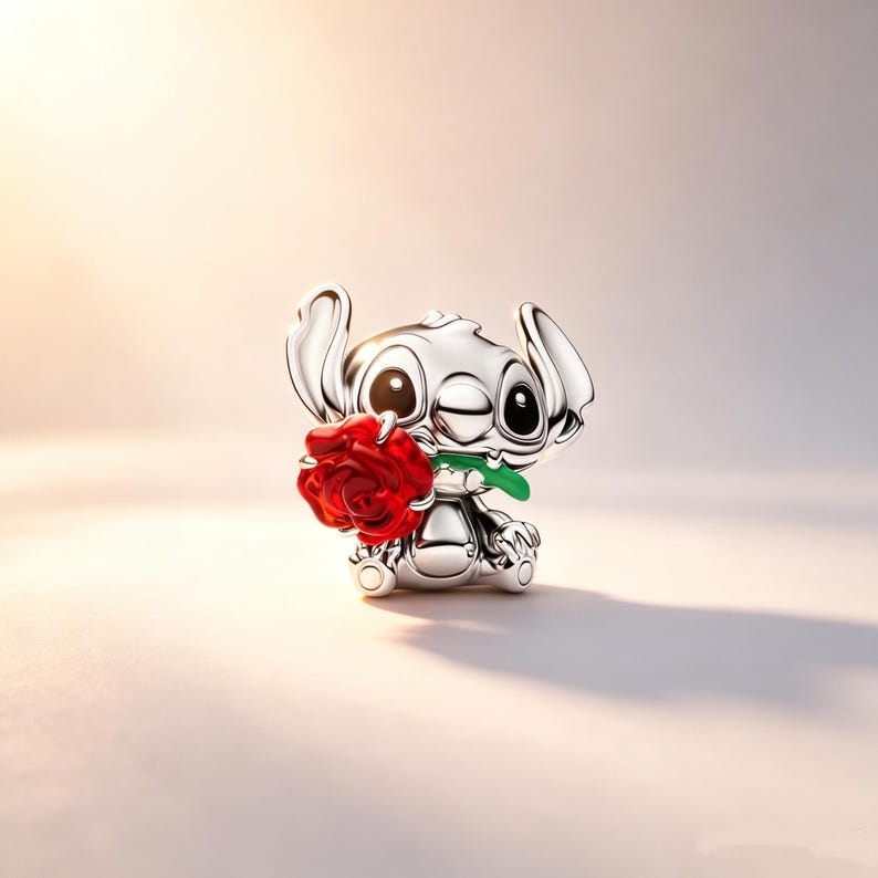 Puede incluir: Una figura plateada del personaje Stitch de Lilo & Stitch, sosteniendo una rosa roja con un tallo verde. La figura gui&ntilde;a un ojo y tiene ojos grandes y expresivos. La rosa est&aacute; detallada con p&eacute;talos visibles.