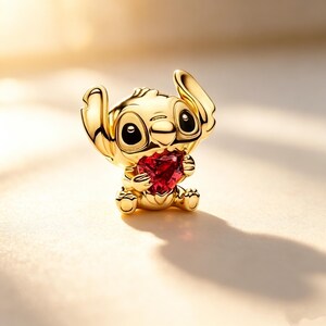Puede incluir: Una figura dorada del personaje Stitch, sosteniendo una gema roja en forma de coraz&oacute;n. La figura tiene ojos negros grandes y orejas grandes. El fondo es un degradado de luz suave y borroso.