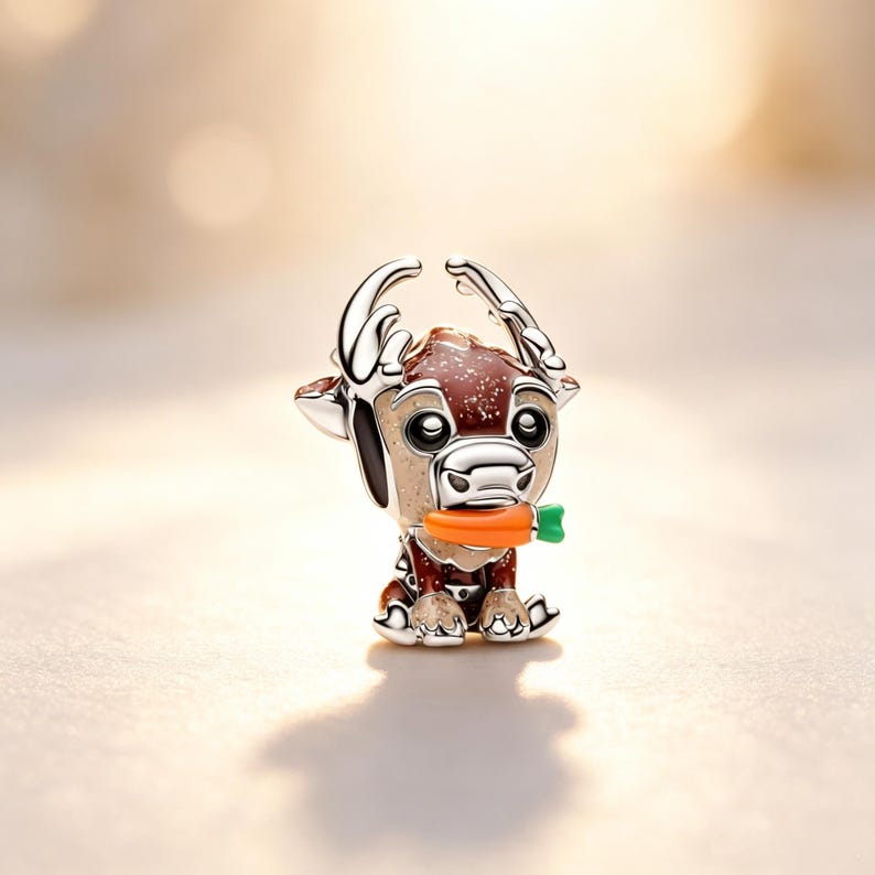 Puede incluir: Un charm plateado con forma de reno, sosteniendo una zanahoria naranja con la parte superior verde. El reno tiene detalles marrones y blancos, con cuernos plateados y un cuerpo moteado marr&oacute;n rojizo. El charm es para un brazalete o collar.