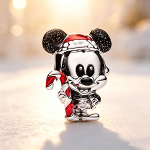 Puede incluir: Un charm de Mickey Mouse plateado con un gorro de Pap&aacute; Noel y un bast&oacute;n de caramelo rojo y blanco. El charm tiene orejas negras con motas blancas, sobre un fondo nevado.