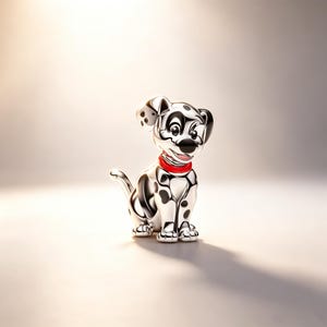 Puede incluir: Figura de d&aacute;lmata plateado con manchas negras y collar rojo. El perro est&aacute; sentado, con la cola enroscada. La figura tiene un acabado brillante y est&aacute; sobre un fondo suave y neutro.
