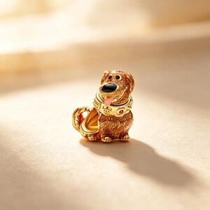 Puede incluir: Figura dorada de perro con cuerpo marr&oacute;n, nariz negra y lengua rosa. El perro lleva un collar dorado con detalles rojos. La figura tiene una expresi&oacute;n sonriente y est&aacute; sobre un fondo suave y neutro.
