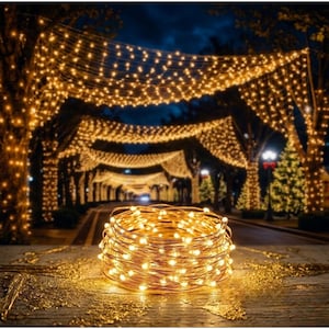May include: A coil of warm white LED string lights sits in front of a pathway lined with trees decorated with similar lights. The lights are strung overhead, creating a festive, illuminated tunnel effect. The scene is set at dusk.