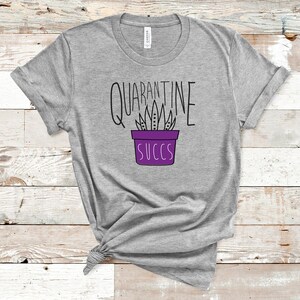 May include: Grey t-shirt with a purple succulent plant illustration and the text "Quarantine Succs".