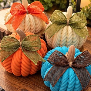May include: Four decorative pumpkin-shaped items featuring a braided texture and a stem. Each pumpkin is adorned with a burlap ribbon bow. The colors include white with an orange bow, white with a green bow, orange with a green bow, and blue with a brown bow.