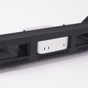 May include: A black rack mount enclosure with a white device in the center. The enclosure has openings on each side and a series of ventilation slots. The device has two small holes and a series of ventilation slots.