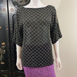 May include: A black sheer top with a gold sequin pattern. The top has a scoop neck and short sleeves.