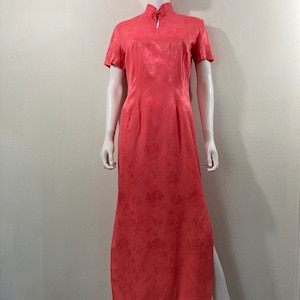 May include: A long, pink, floral print dress with a mandarin collar and short sleeves. The dress has a side slit and is made of a silky fabric.