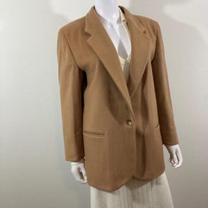 May include: A camel-colored blazer with a single button closure and a notched lapel. The blazer has a smooth, textured fabric and a relaxed fit.