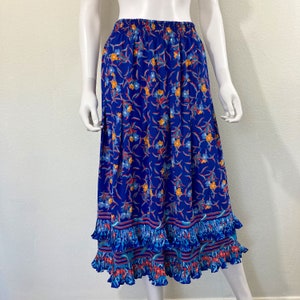May include: A blue floral skirt with an elastic waistband and a tiered ruffle hem. The skirt features a vibrant pattern of orange, blue, and red flowers and leaves against a deep blue background. The skirt is knee-length.