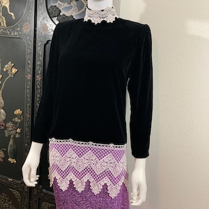May include: Black velvet blouse with a white lace collar and trim. The blouse has long sleeves and a mock neck.