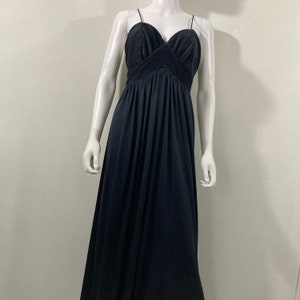 May include: A black evening gown on a mannequin. The dress features a pleated bodice with a sweetheart neckline and thin spaghetti straps. The skirt flows to the floor. The dress is made of a soft, flowing fabric.