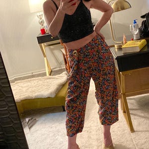 May include: Black sequined crop top paired with floral print culottes. The culottes feature a vibrant pattern of red, orange, and blue flowers on a black background. Gold-colored heeled sandals complete the outfit, creating a stylish ensemble.