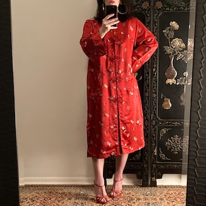 May include: A long red satin robe with floral embroidery and a mandarin collar. The robe has a front closure with decorative buttons.