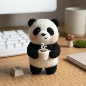 May include: A handcrafted panda figurine with black and white fur, holding a small white cup with a brown beverage. The panda has rosy cheeks and black eyes. The figurine is on a wooden surface.