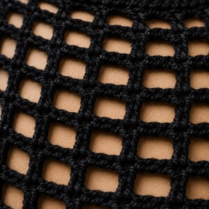 May include: A black crochet garment featuring a distinct open-work grid pattern. The textile is constructed from thick, dark yarn loops that form uniform square openings, revealing a solid tan-coloured layer underneath the textured surface.