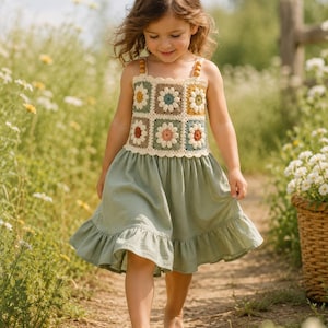 Può includere: Un vestito con corpetto all'uncinetto composto da motivi quadrati a fiori nei toni del bianco, giallo, blu e marrone, abbinato a una gonna verde salvia tinta unita con orlo a balze e spalline sottili decorate con perline di legno.