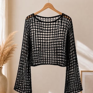 May include: A black long-sleeve top featuring an open-knit crochet construction with a grid-like pattern. The garment has a wide, rounded neckline and flared sleeves that extend from the shoulders, creating a loose, airy silhouette throughout.