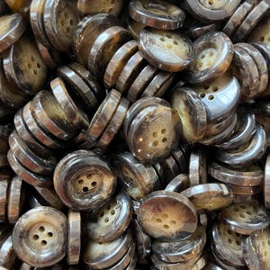 May include: A close-up of a collection of brown buttons, each with four holes. The buttons have a marbled effect, displaying shades of brown and tan. The buttons are round with a slightly raised edge.