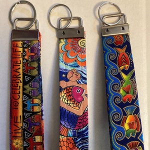May include: Three colorful keychains with silver key rings. The keychains feature different designs: one with a colorful fish and mermaid, one with a colorful floral design, and one with a blue and gold design with the text "LIVE CELEBRATE LIFE".