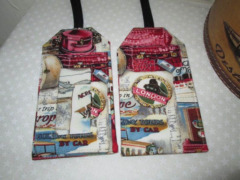 May include: Two luggage tags with a vintage travel theme. The tags are made of fabric and feature a red suitcase, a plane, and a map. The text on the tags reads "Holiday Tours by Car" and "Across the World".