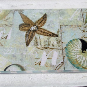 May include: A decorative fabric with a blue, green, and brown floral pattern. The fabric features a stylized flower with a brown center and a seashell with a black center.