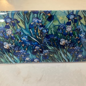 May include: A rectangular card or print encased in a clear plastic sleeve, featuring a vibrant, detailed illustration of blue and purple iris flowers with long green leaves, set against a soft, light green and yellow background.