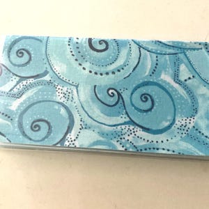 May include: A blue checkbook cover with a swirling pattern of white and blue. The pattern resembles clouds or water.