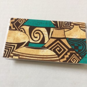 May include: A close-up of a fabric with a pattern of brown and teal pottery. The pottery is decorated with geometric designs.