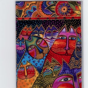 May include: A vibrant fabric panel with a design of stylized cat faces. The cats are depicted in red, orange, blue, and purple, with gold detailing. The artwork is encased in a clear plastic frame.