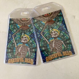 May include: Two clear plastic luggage tags with a tie-dye background featuring a skeleton holding a bird and the text "Grateful Dead".