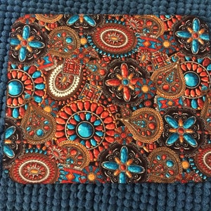 Puede incluir: Una alfombrilla de ratón de tela marrón con un patrón colorido de formas geométricas turquesa, naranja y dorado. El patrón se asemeja a un mosaico de joyas.