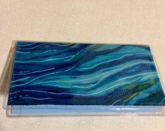 May include: A clear plastic checkbook cover with a blue and green watercolor-style design of wavy lines.