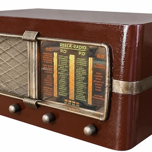 May include: A vintage-style brown radio with a glossy finish, featuring a rectangular dial labelled REELA-RADIO with various city names, a metallic speaker grille on the left, and four silver control knobs along the bottom front edge.