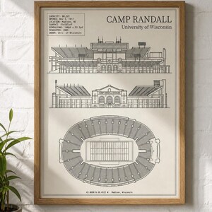 Op de afbeelding: Een ingelijste architecturale print van het Camp Randall Stadion van de University of Wisconsin. Het kunstwerk toont zwarte lijntekeningen van het stadion vanuit drie perspectieven, inclusief een bovenaanzicht, met tekstdetails over de faciliteit.