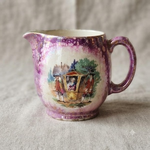 May include: A ceramic creamer featuring a mottled purple and gold luster glaze. The center panel displays a colorful illustration of a person seated in a sedan chair carried by two figures in historical attire, set against a landscape background.