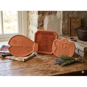 Può includere: Tre stampi da cucina in terracotta con forme e texture distinte. Uno stampo ha la forma di un pesce, uno è quadrato con un motivo a griglia e uno è rotondo e raffigura un gallo. Questi oggetti in argilla non smaltata hanno una finitura opaca.